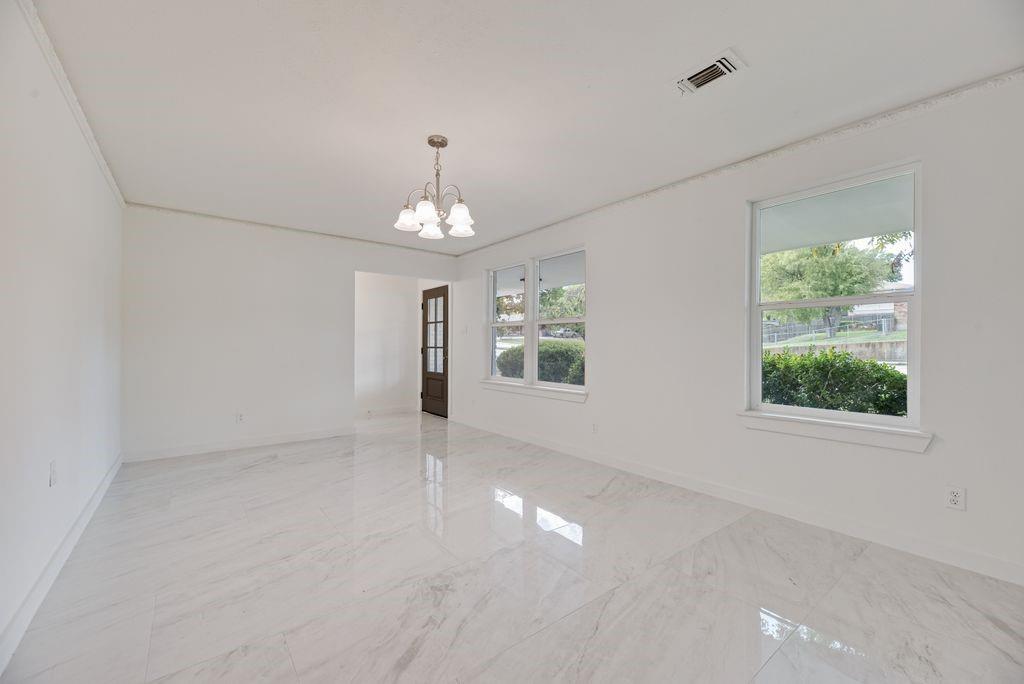 Grand room could be living and dining,  featuring polished large-format tile flooring, multi-pane glass entry door, and multi-light chandelier