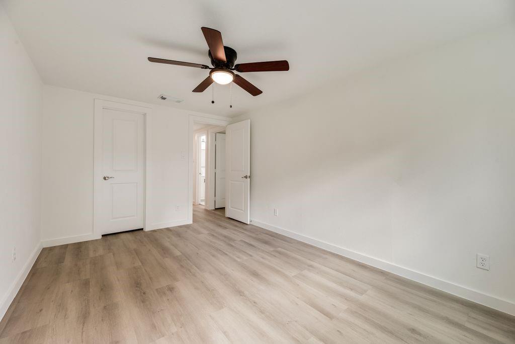 Room featuring wood-finish flooring, a central ceiling fan with integrated lighting, and two-panel interior doors