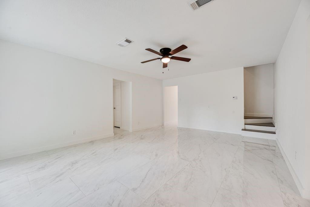 Open-concept interior featuring large-format tile flooring with a neutral veining pattern, a central multi-blade ceiling fan, and architectural staircase steps with dark-finish treads