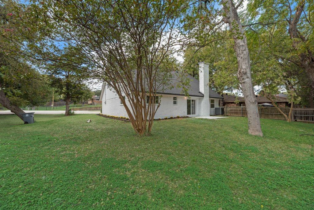Exterior white-painted brick facade, gabled roofline, central chimney, sliding glass door, and expansive backyard with mature trees