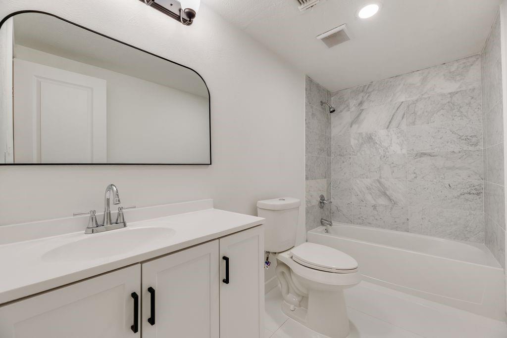 Bathroom featuring a vanity with a white countertop and integrated sink, arch-top wall mirror, matte black hardware, and a tub with surround tile