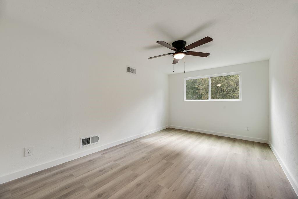 Room featuring wood-finish flooring, white walls, and a ceiling-mounted light fixture with a fan