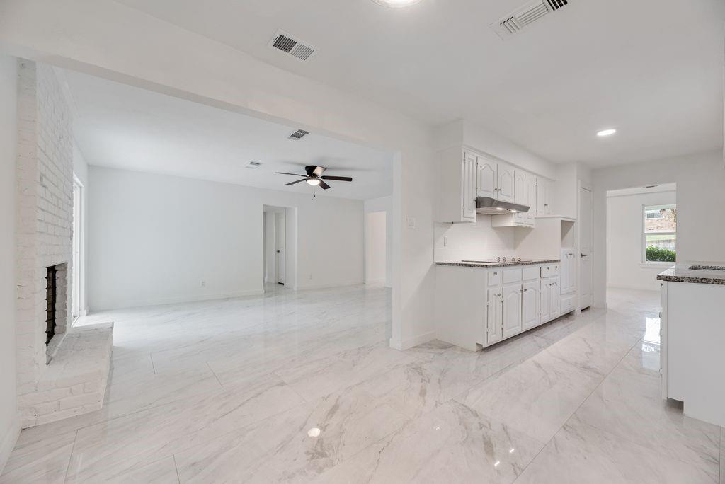 Open-concept interior featuring large-format tile flooring, a painted brick fireplace, white cabinetry, recessed lighting, and a ceiling fan Open-concept interior featuring large-format tile flooring, a painted brick fireplace, white cabinetry, recessed lighting, and a ceiling fan