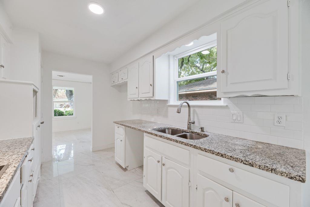 Kitchen featuring white cabinetry, stone-finish countertops, subway tile backsplash, dual-basin stainless steel sink with gooseneck faucet, and light-tone tile flooring
