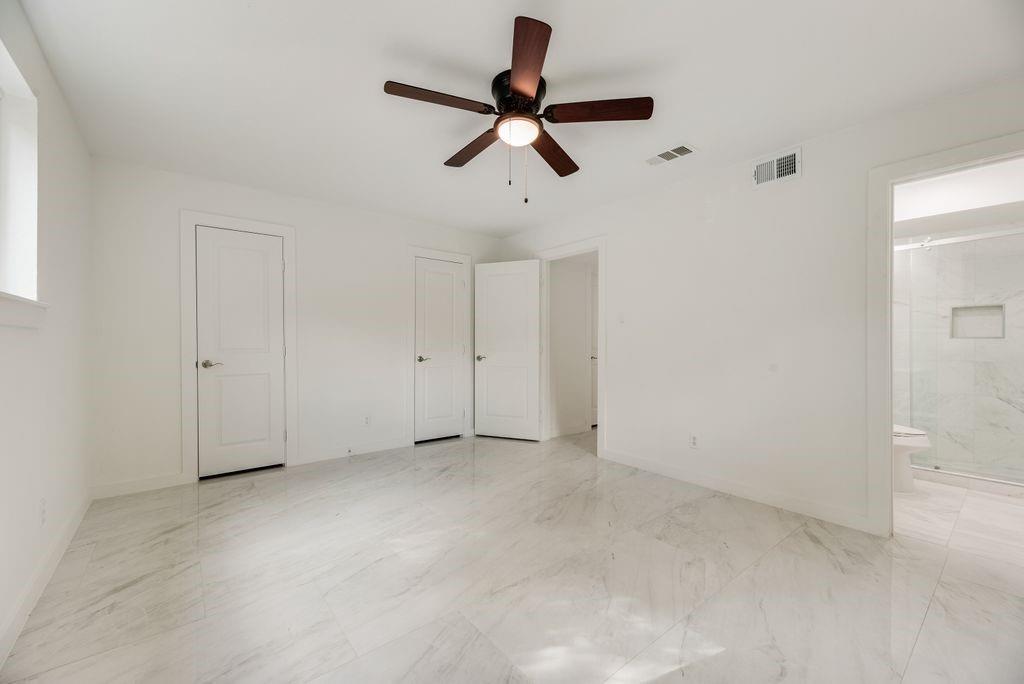 Primary Bedroom 2, Spacious room featuring large-format stone-style flooring, a central ceiling fan with integrated lighting, and three panel doors Primary Bedroom 2, Spacious room featuring large-format stone-style flooring, a central ceiling fan with integrated lighting, and three panel doors