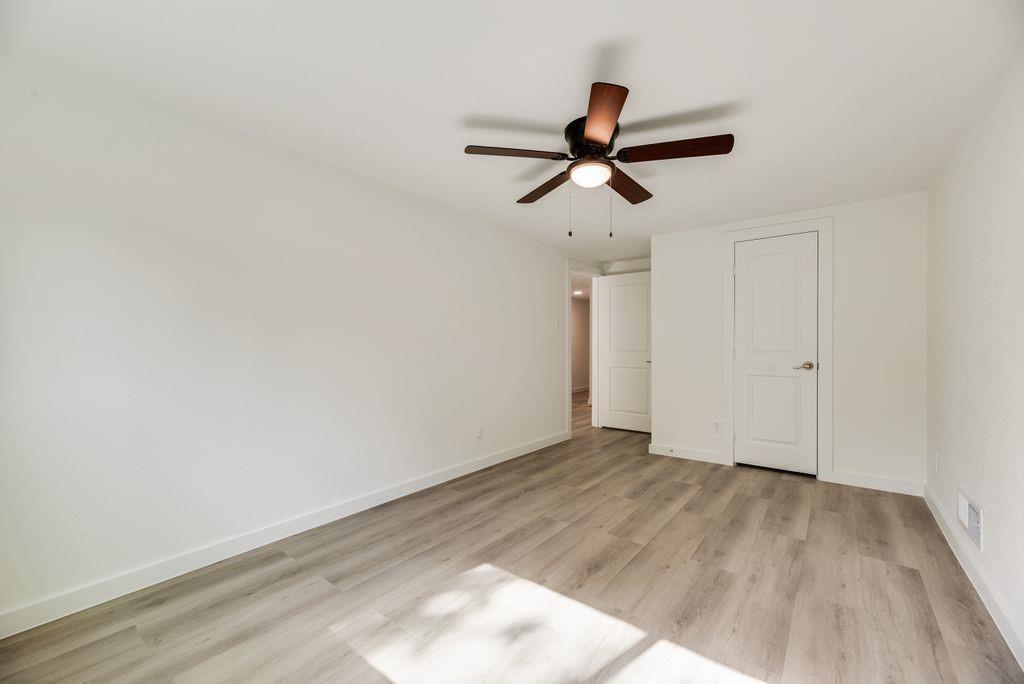 Interior space featuring neutral wall paint, wood-finish flooring, a ceiling-mounted fan with integrated light fixture, and two-panel interior doors