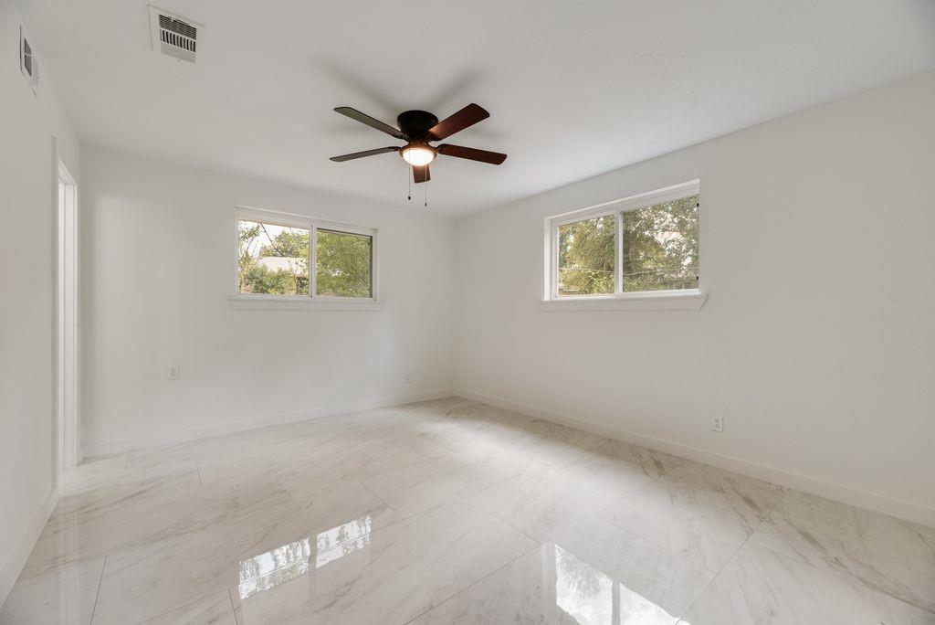 Polished stone-finish flooring, dual windows, and a central ceiling fan with integrated light fixture