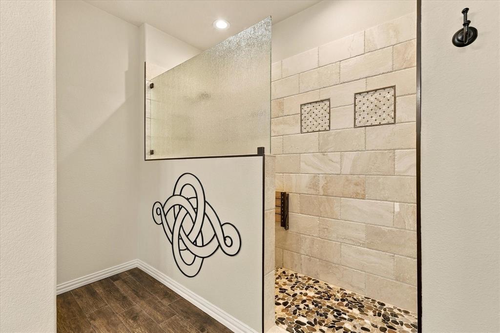Indulge in a spa-like experience with this custom 8 foot walk-in shower, featuring beautiful tilework, a pebble stone floor, and sleek frameless glass.