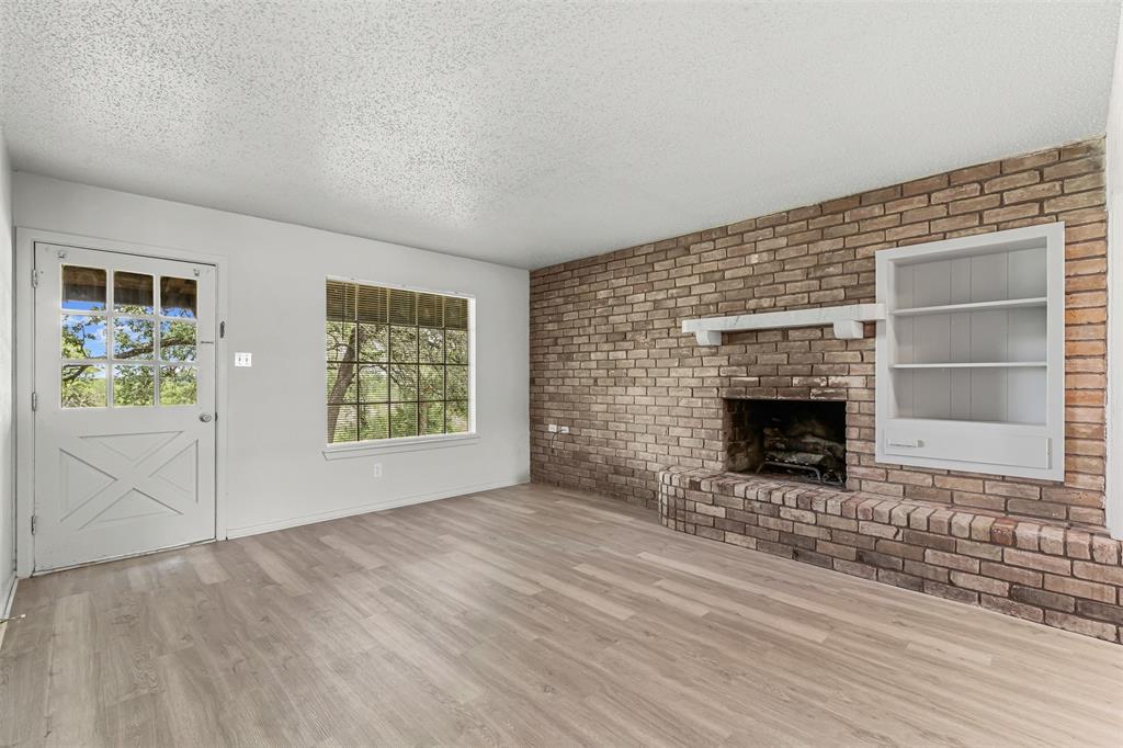 Unfurnished living room featuring a textured ceiling, wood finished floors, a brick fireplace, and brick wall