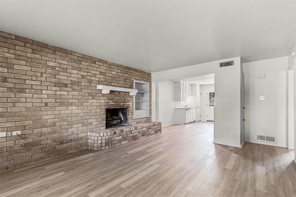 Unfurnished living room featuring a textured ceiling, light wood-style floors, brick wall, and a brick fireplace