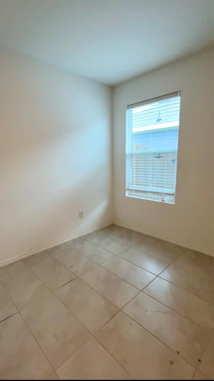Room featuring large-format tile flooring, smooth white walls, and a single window with horizontal blinds