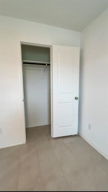 Neutral-toned tile flooring, two-panel interior door, and integrated closet with overhead shelf and hanging rod