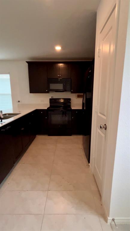 Kitchen featuring dark cabinetry, solid-surface countertops, black appliances, and large-format tile flooring