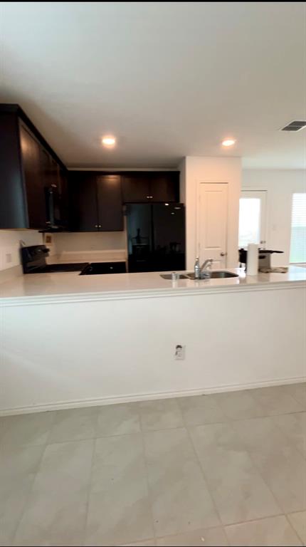 Kitchen featuring dark wood cabinetry, solid surface countertops, a stainless steel sink with a chrome faucet, and tiled flooring