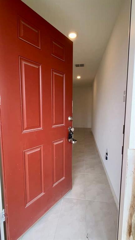 Red six-panel entry door with metallic hardware, large-format tile flooring, and recessed ceiling lighting