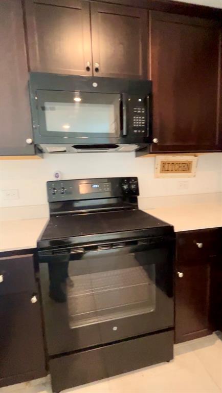 Dark-toned cabinetry featuring a built-in over-the-range microwave and a freestanding electric range with a glass-ceramic cooktop, complemented by light-toned countertops