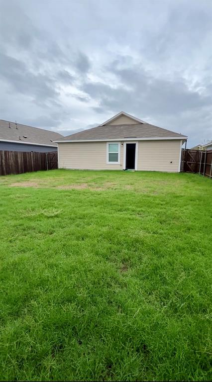 Backyard featuring a grass lawn, perimeter wood fencing, and a gable roof exterior