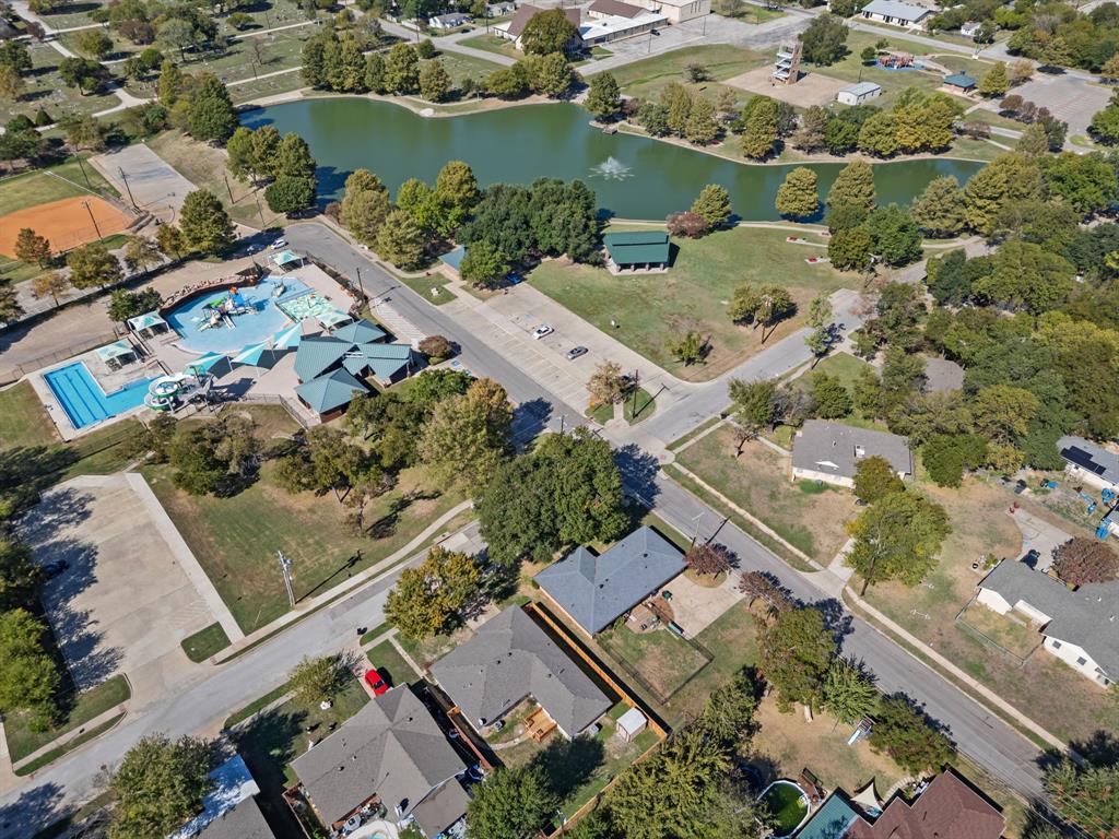 Aerial perspective showcasing a residential community with proximity to a public park featuring a pond, swimming pool, water play area, and recreational facilities Aerial perspective showcasing a residential community with proximity to a public park featuring a pond, swimming pool, water play area, and recreational facilities