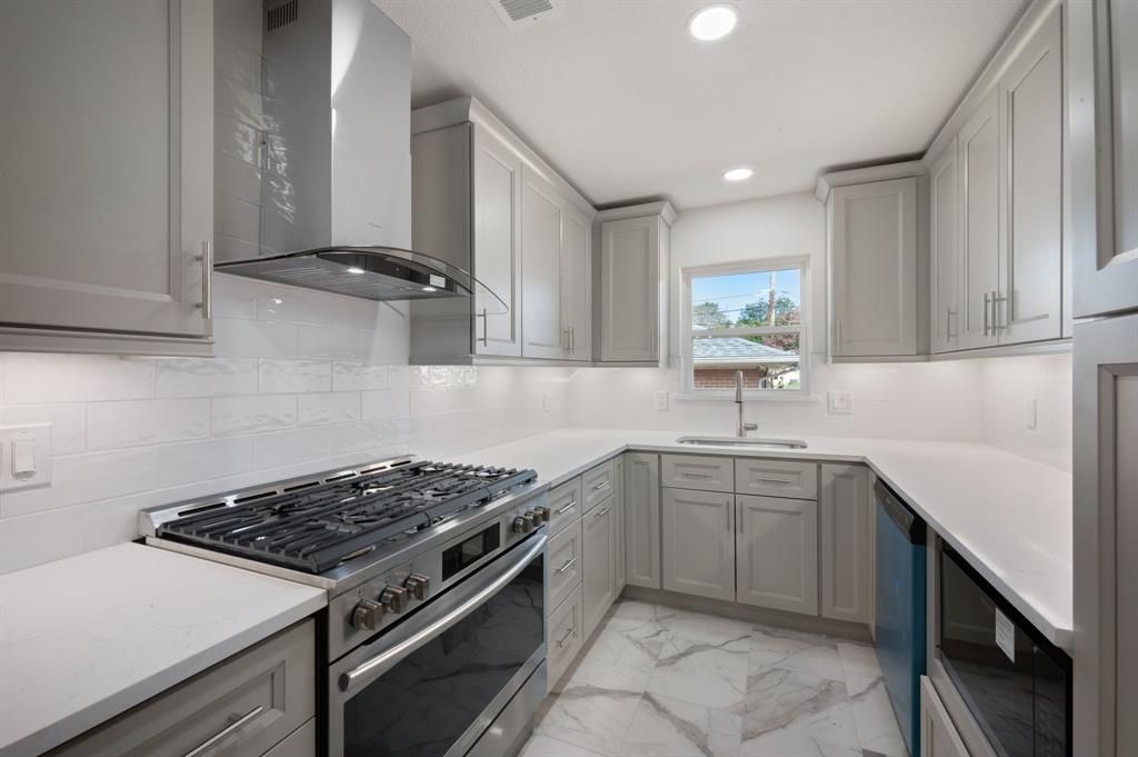 Kitchen featuring light-gray shaker cabinetry, quartz countertops, white subway tile backsplash, stainless steel gas range with a chimney-style hood, and stone-finish flooring