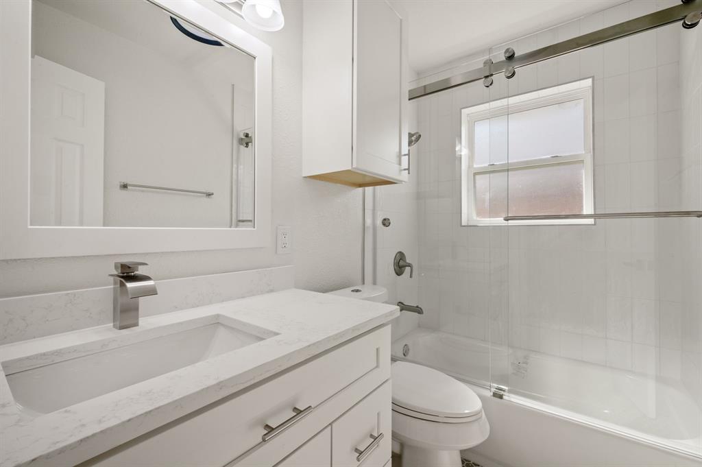 Bathroom featuring a white vanity with a composite countertop, undermount sink, sliding glass shower enclosure, and white wall-mounted cabinetry