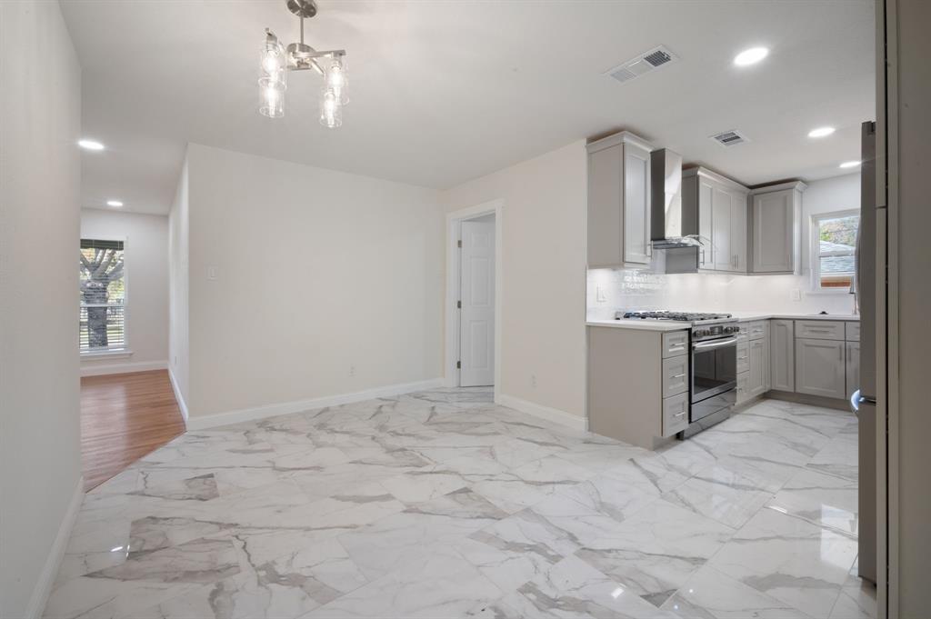 Kitchen featuring large-format tile flooring with marble-pattern veining, shaker-style cabinetry, stainless steel gas range, built-in range hood, and recessed lighting