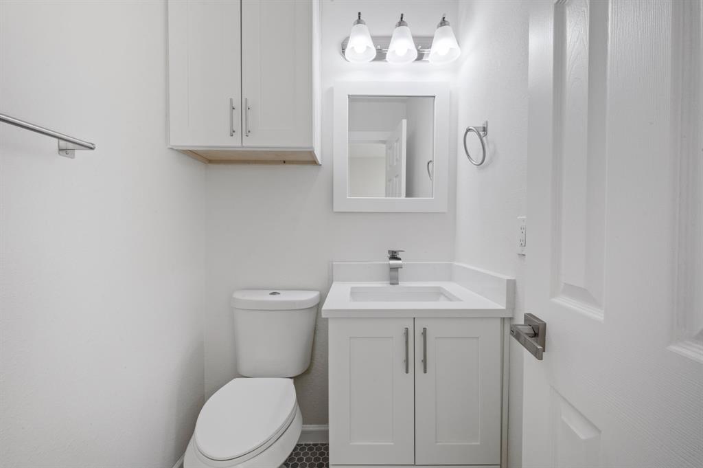 White cabinetry, vanity with integrated countertop, three-light fixture, wall-mounted mirror, and hexagonal floor tile