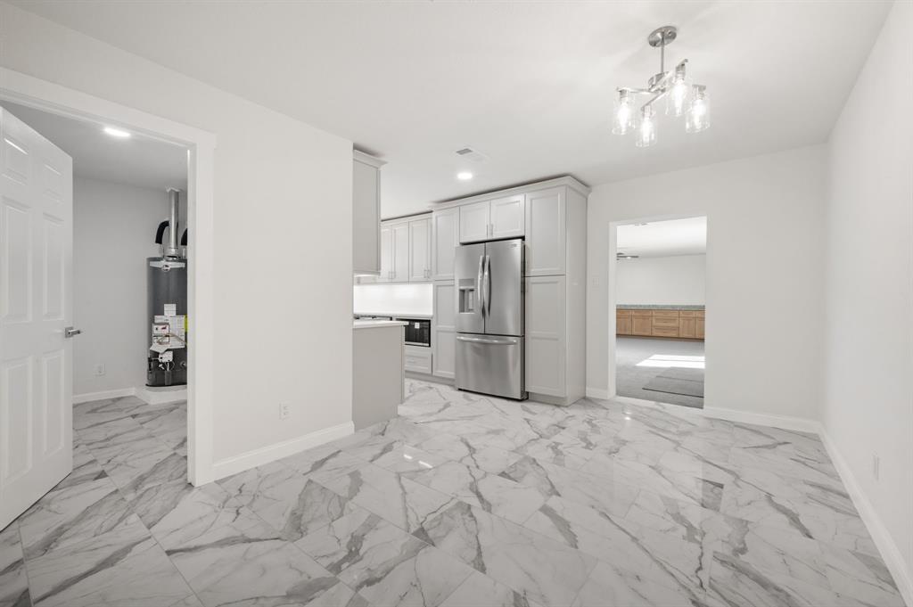 Kitchen featuring stone-pattern tile flooring, shaker-style cabinetry, stainless steel refrigerator, and polished multi-light chandelier Kitchen featuring stone-pattern tile flooring, shaker-style cabinetry, stainless steel refrigerator, and polished multi-light chandelier