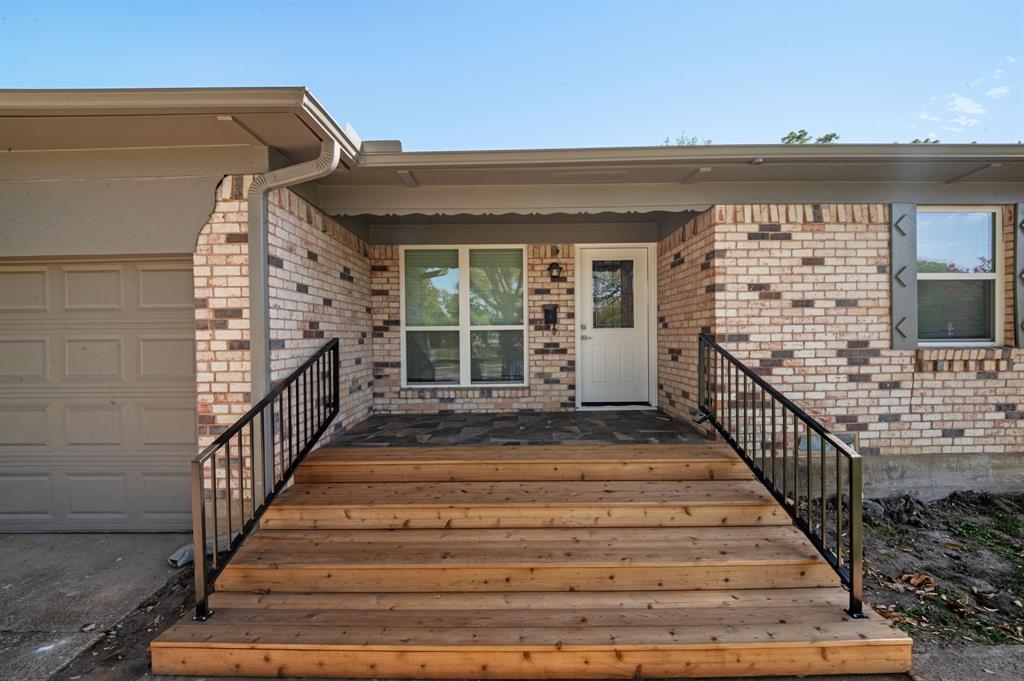 Brick exterior featuring natural wood-finish front steps, flagstone porch flooring, and black metal handrails Brick exterior featuring natural wood-finish front steps, flagstone porch flooring, and black metal handrails
