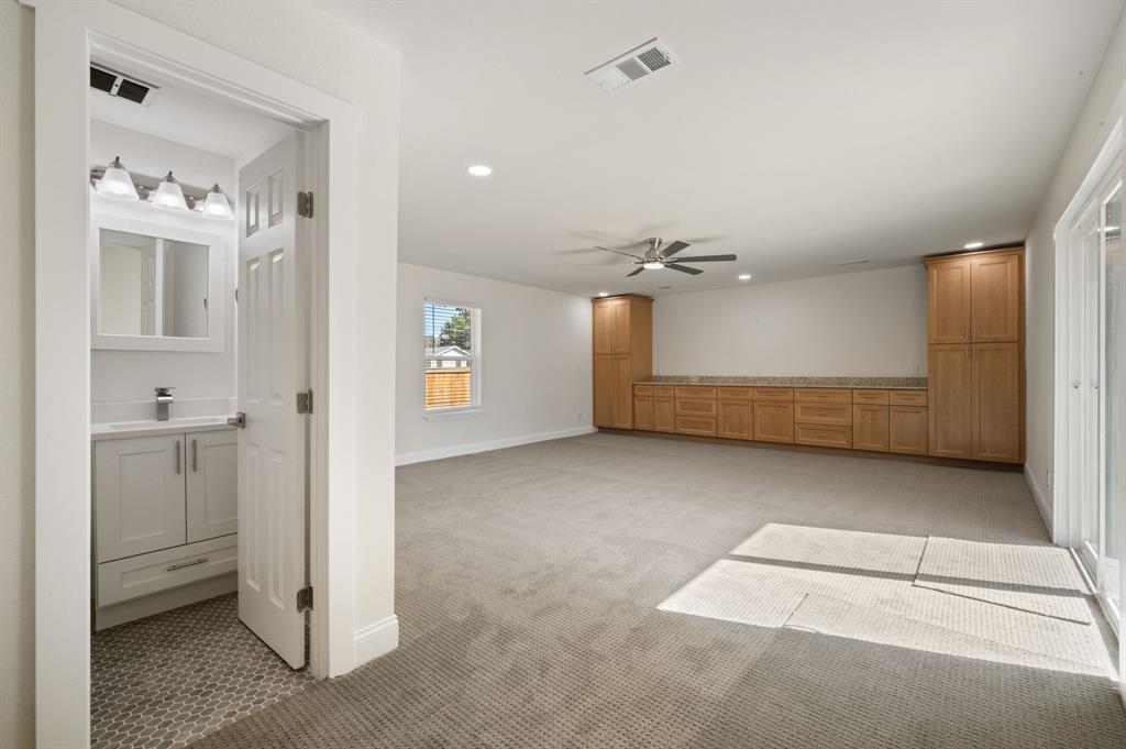 Room featuring wall-to-wall carpeting, extensive built-in cabinetry with stone-finish countertops, recessed lighting, and a bathroom containing a vanity with a sink and a decorative tile floor