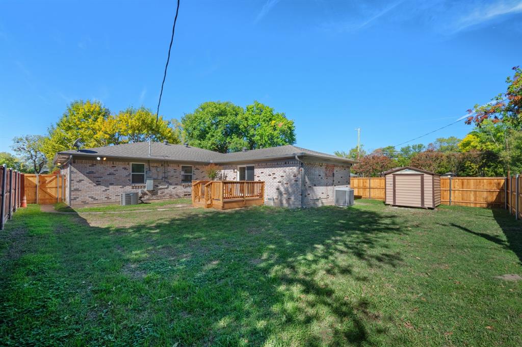 Backyard featuring a brick exterior, raised wood deck, wood privacy fencing, and a detached storage structure