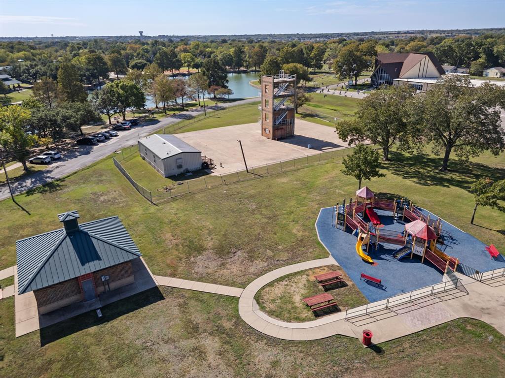 Outdoor recreational area featuring a playground with rubberized surfacing, a detached structure with a metal roof, concrete walkways, and open green space Outdoor recreational area featuring a playground with rubberized surfacing, a detached structure with a metal roof, concrete walkways, and open green space