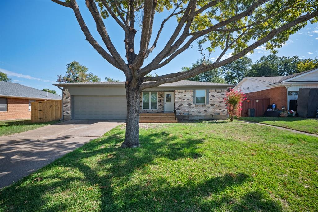 Single-story exterior featuring a brick facade, attached two-car garage, wood-finish front steps, and a concrete driveway