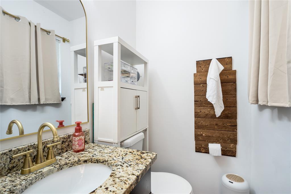 Bathroom featuring a stone countertop with an undermount sink, a brass-finish dual-handle faucet, and an arched wall mirror Bathroom featuring a stone countertop with an undermount sink, a brass-finish dual-handle faucet, and an arched wall mirror