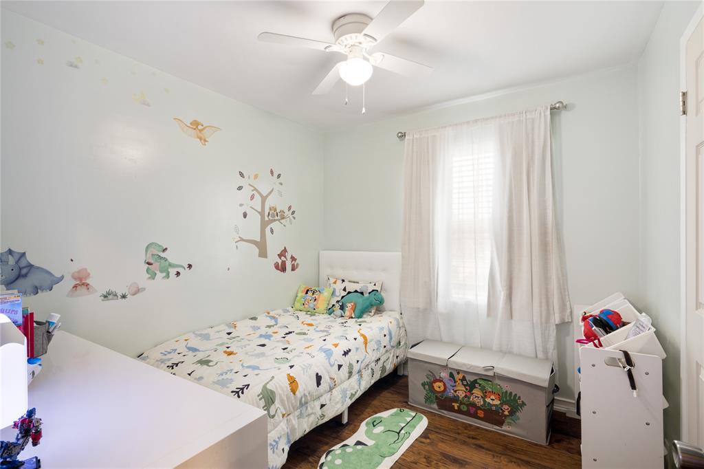 Bedroom featuring wood-finish flooring, a white ceiling fan with integrated lighting, and a window with hardware for window treatments
