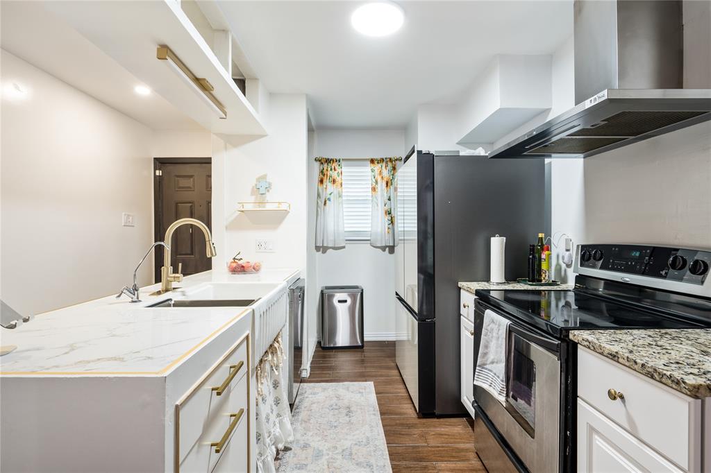 Kitchen featuring an apron-front sink, gold-tone faucet, stone-surfaced countertops, stainless steel appliances, and wood-finish flooring Kitchen featuring an apron-front sink, gold-tone faucet, stone-surfaced countertops, stainless steel appliances, and wood-finish flooring