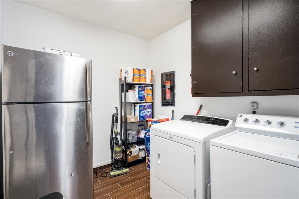 Utility space featuring wood-finish tile flooring, wall-mounted dark cabinetry, and a full-size stainless steel refrigerator