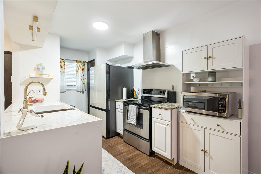 Kitchen featuring wood-finish flooring, white cabinetry, stone-patterned countertops, a stainless steel chimney-style range hood, and a high-arch faucet Kitchen featuring wood-finish flooring, white cabinetry, stone-patterned countertops, a stainless steel chimney-style range hood, and a high-arch faucet