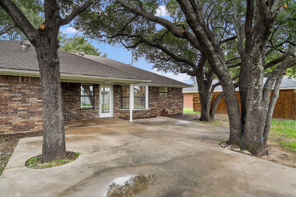 Brick exterior with a concrete patio, mature trees, and wood-paneled fencing