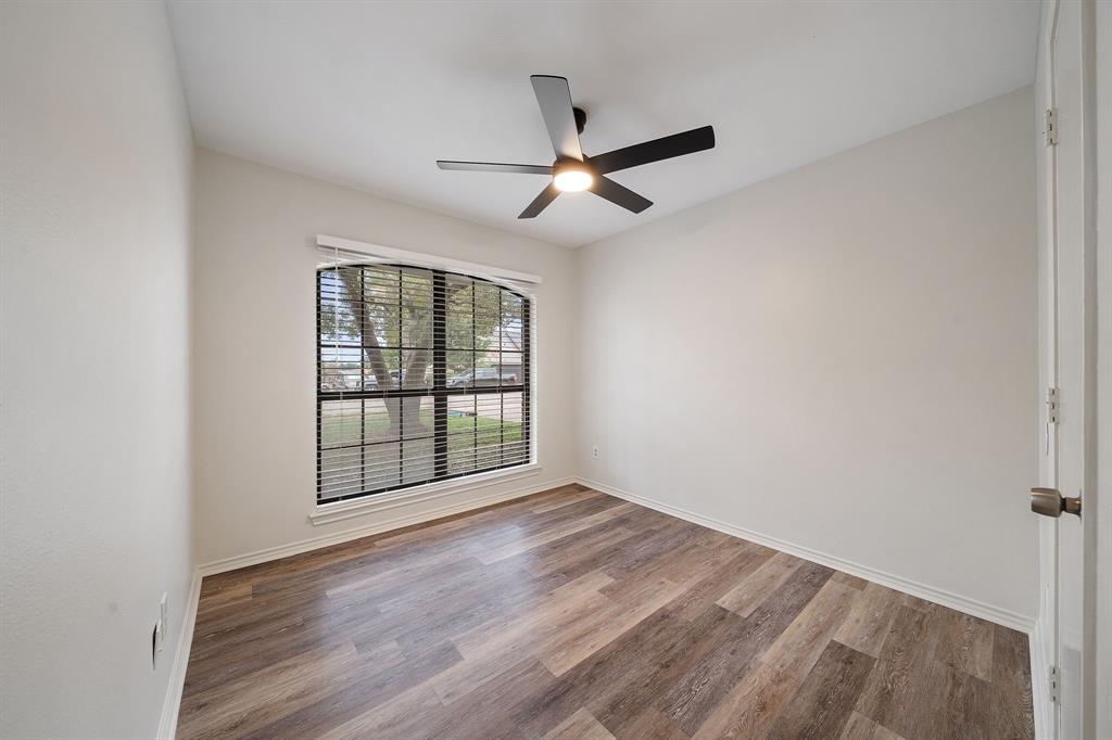 Room featuring wood-finish flooring, a matte black ceiling fan with integrated lighting, and a large arched window with grid mullions