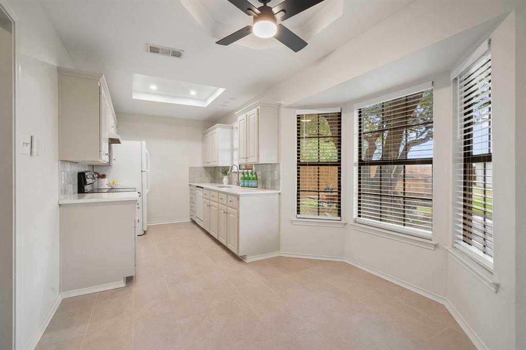 Kitchen featuring neutral cabinetry, quartz countertops, tile flooring, tray ceiling with integrated lighting, and dining area with a bay window Kitchen featuring neutral cabinetry, quartz countertops, tile flooring, tray ceiling with integrated lighting, and dining area with a bay window