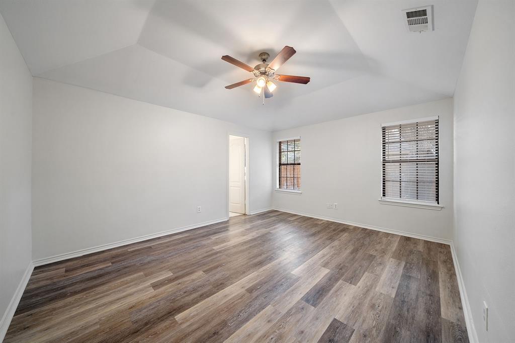 Room featuring tray ceilings, wood-finish flooring, and a ceiling fan with integrated lighting