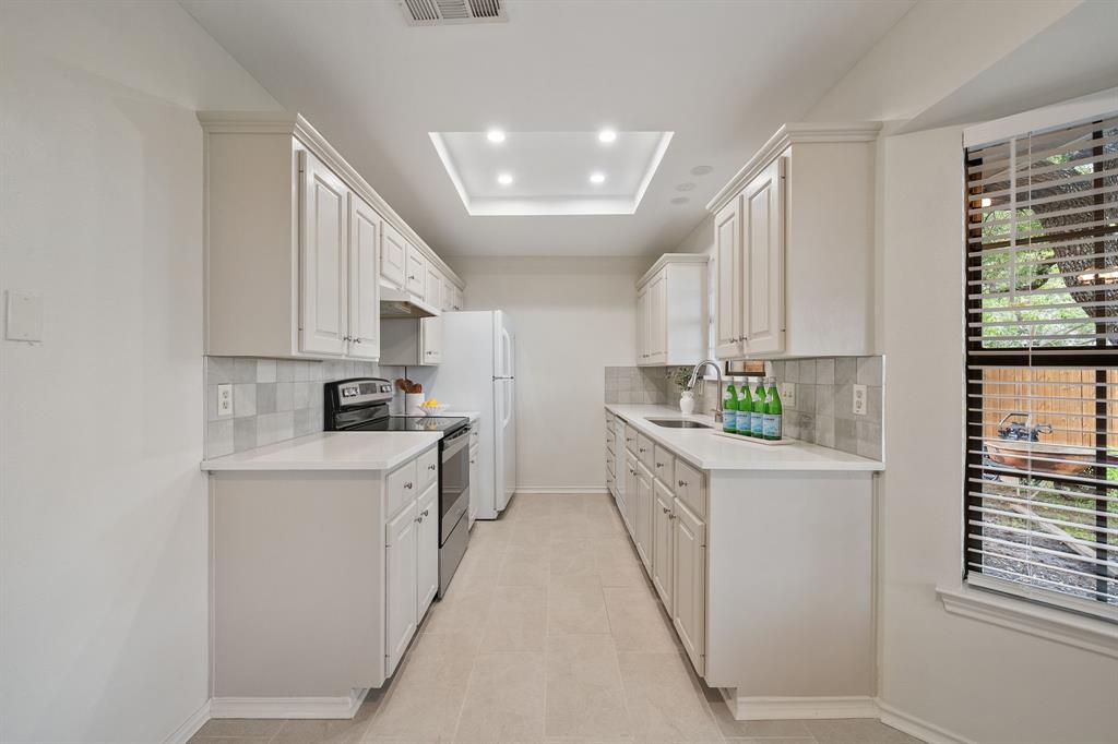 Kitchen featuring off-white cabinetry, solid-surface countertops, tile backsplash, tile flooring, and a recessed ceiling light fixture Kitchen featuring off-white cabinetry, solid-surface countertops, tile backsplash, tile flooring, and a recessed ceiling light fixture