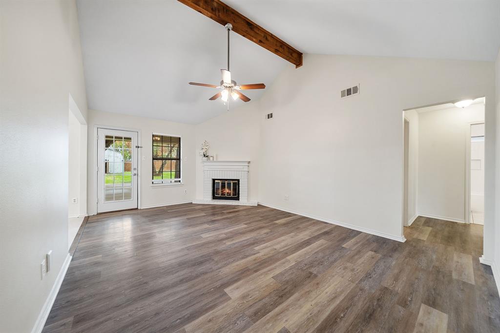 Vaulted ceiling with an exposed wood beam, wood-finish flooring, and a white masonry fireplace Vaulted ceiling with an exposed wood beam, wood-finish flooring, and a white masonry fireplace