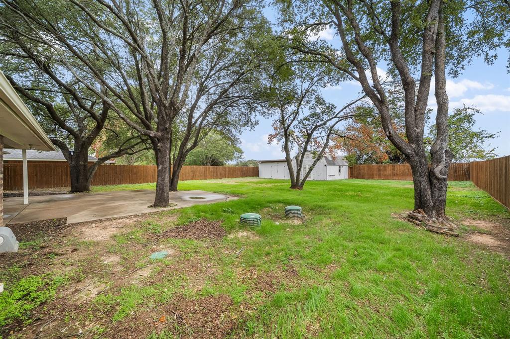 Expansive backyard featuring a concrete patio, mature trees, and perimeter wood fencing