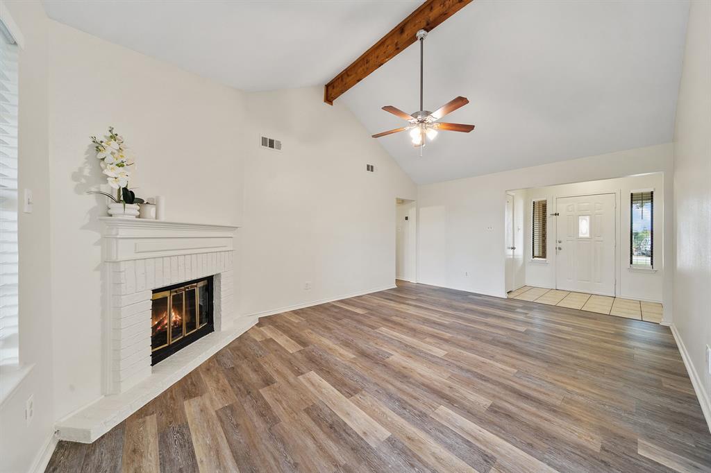 Vaulted ceiling featuring an exposed wood beam, fireplace with a painted brick surround, and LVP flooring Vaulted ceiling featuring an exposed wood beam, fireplace with a painted brick surround, and LVP flooring