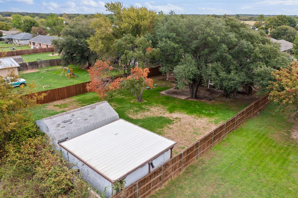 Expansive backyard featuring mature shade trees, a detached storage building with a metal roof, and wood-style privacy fencing