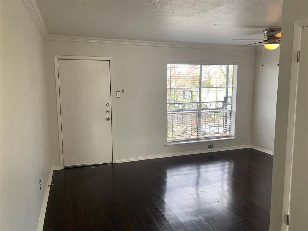 Dark wood-finish flooring, neutral walls, crown molding, a multi-pane window with installed blinds, and a ceiling fan with integrated lighting