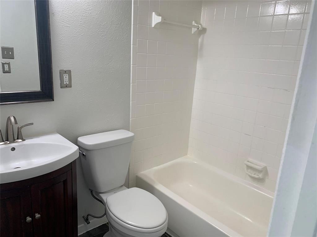 Bathroom featuring a dark wood-finish vanity, white basin sink with a curved faucet, white tile shower surround, and integrated soap dish