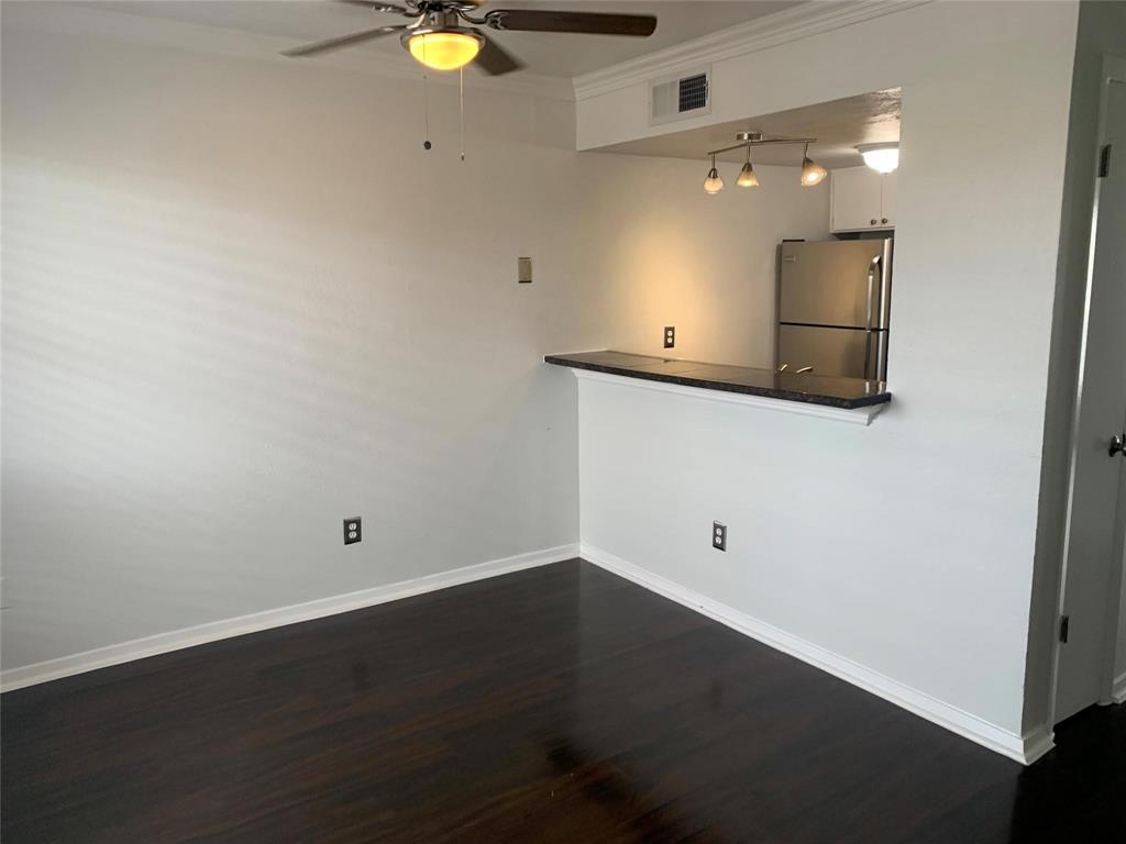 Dark wood-finish flooring, ceiling fan with integrated lighting, pass-through breakfast bar with stone-finish countertop, three-light track lighting fixture, and stainless steel refrigerator