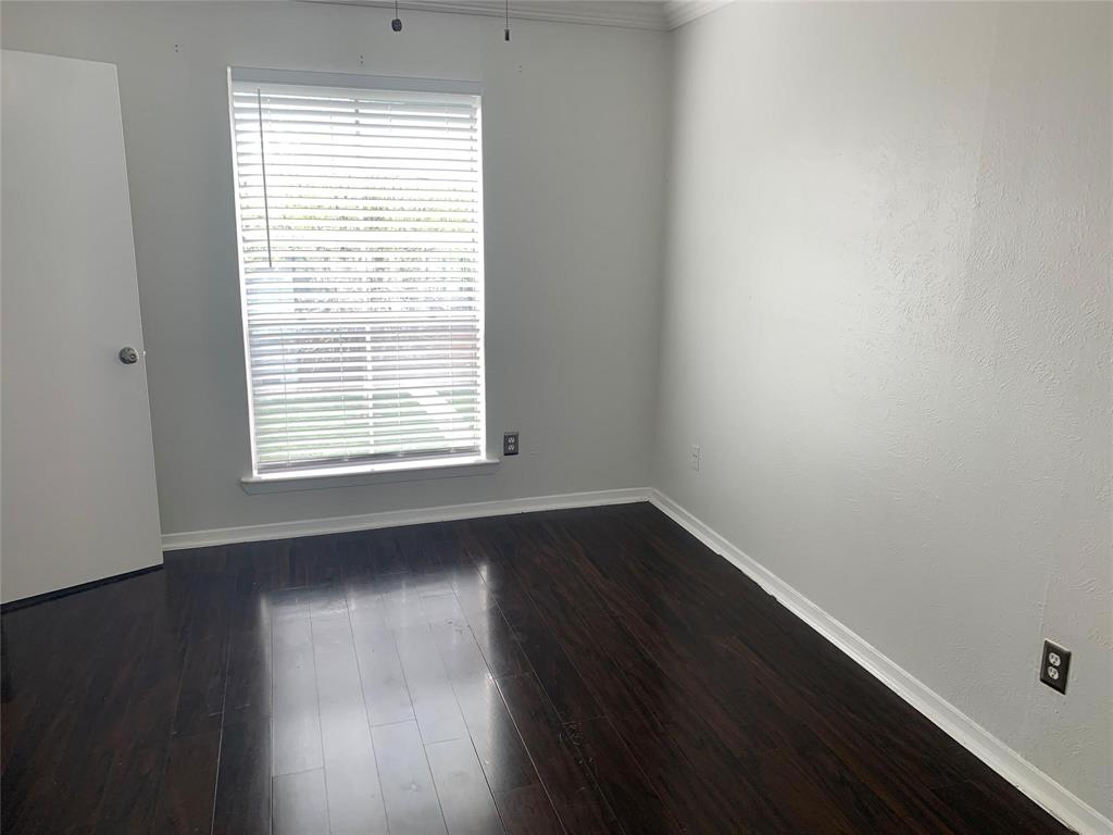 Room featuring dark wood-finish flooring, light-toned wall paint, crown molding, and a window with horizontal blinds